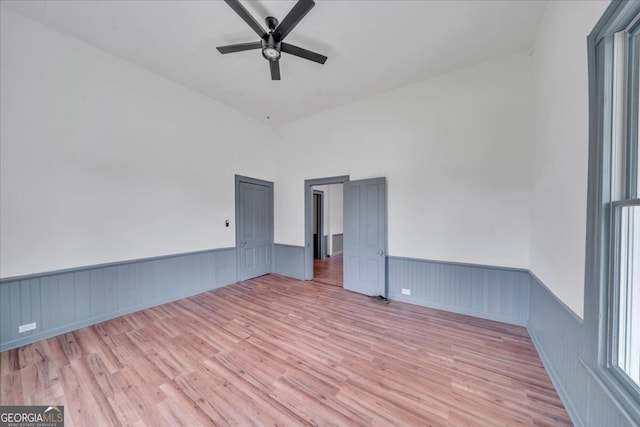 empty room featuring ceiling fan, light wood-type flooring, and wainscoting