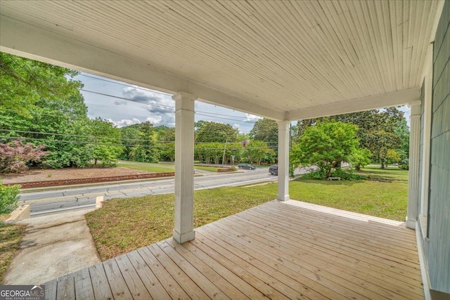 deck with covered porch, a lawn, and view of wooded area