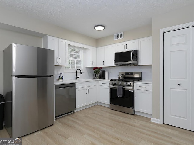 201 Twin Pines Ct, Dallas, GA 30132 - kitchen featuring stainless steel appliances, light countertops, white cabinets, light wood-type flooring, and a textured ceiling