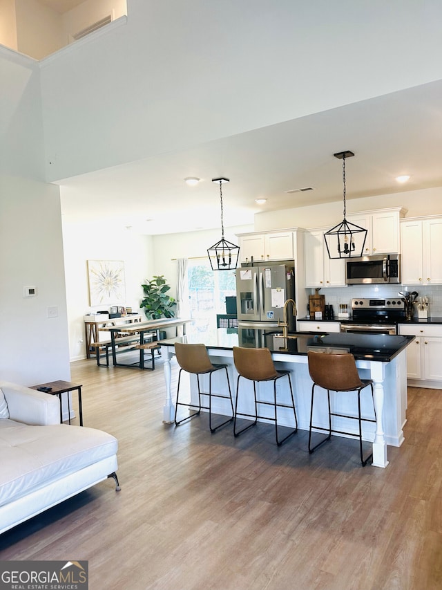 kitchen with stainless steel appliances, an island with sink, dark countertops, white cabinetry, and recessed lighting