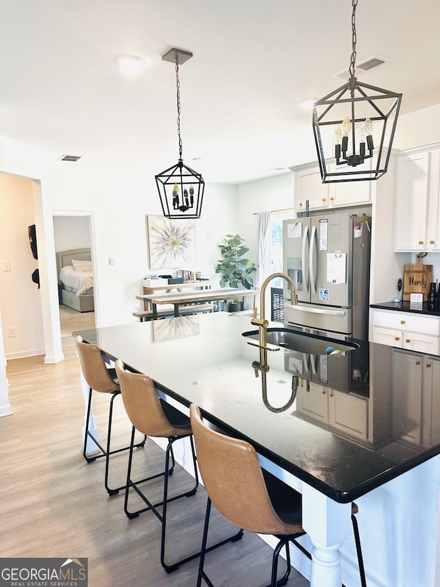 kitchen featuring stainless steel refrigerator with ice dispenser, a chandelier, a sink, white cabinets, and light wood-style floors