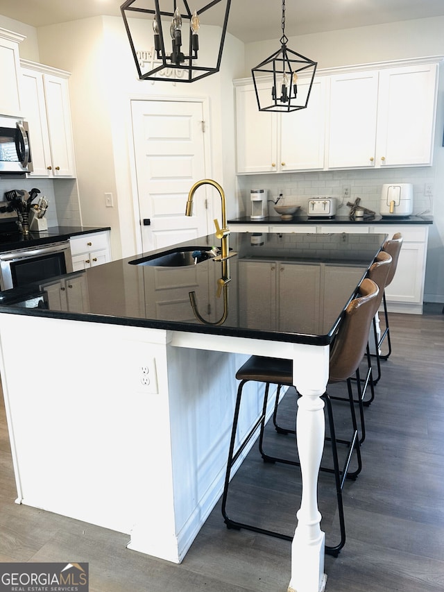 kitchen featuring a sink, dark countertops, stainless steel microwave, backsplash, and dark wood-style flooring