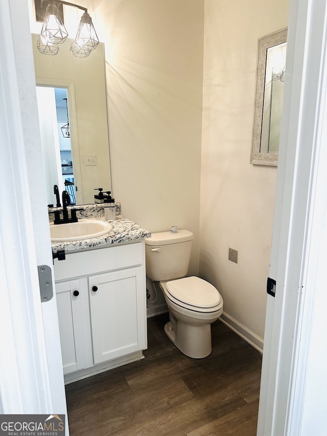 half bath featuring baseboards, wood finished floors, toilet, and vanity