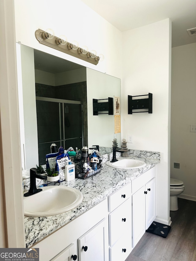 bathroom with wood finished floors, a stall shower, double vanity, toilet, and baseboards