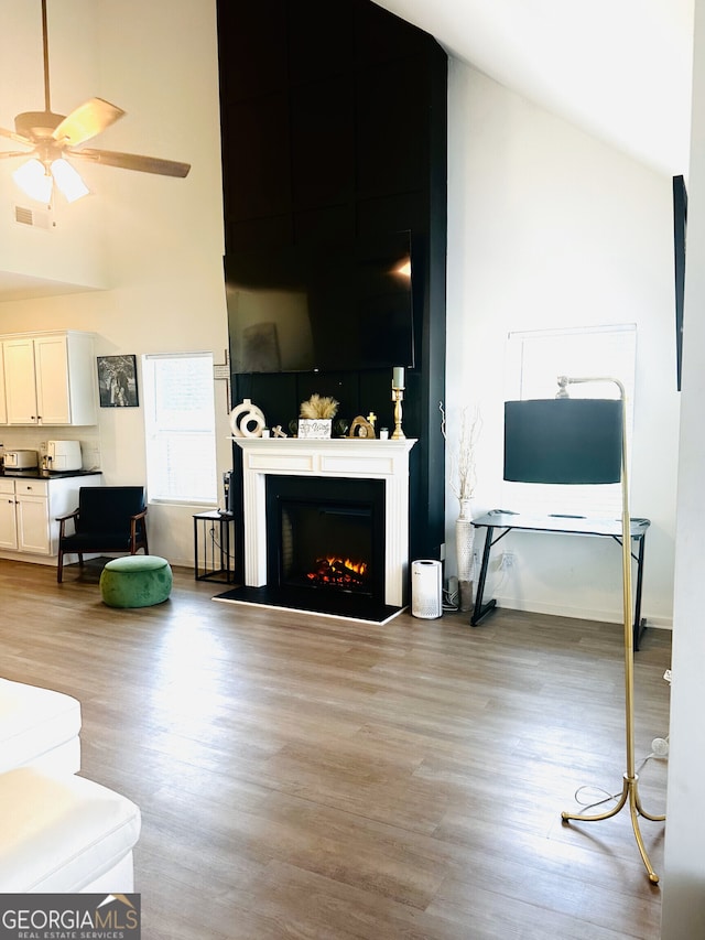 living room with high vaulted ceiling, light wood-type flooring, a ceiling fan, and a warm lit fireplace