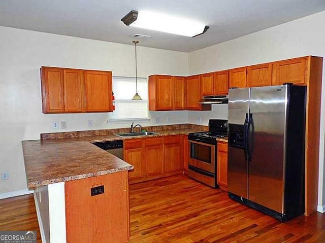 kitchen featuring stainless steel appliances, a peninsula, a sink, under cabinet range hood, and brown cabinetry
