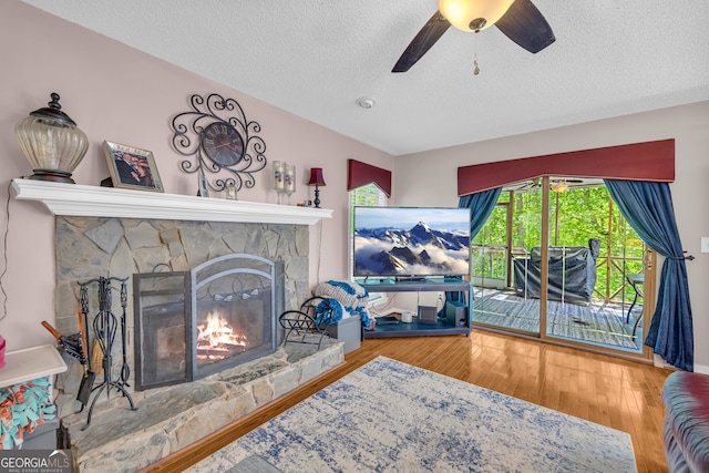 1886 Bend N Hickory Rd, Toccoa, GA 30577 - living room featuring a stone fireplace, a textured ceiling, wood finished floors, and a ceiling fan
