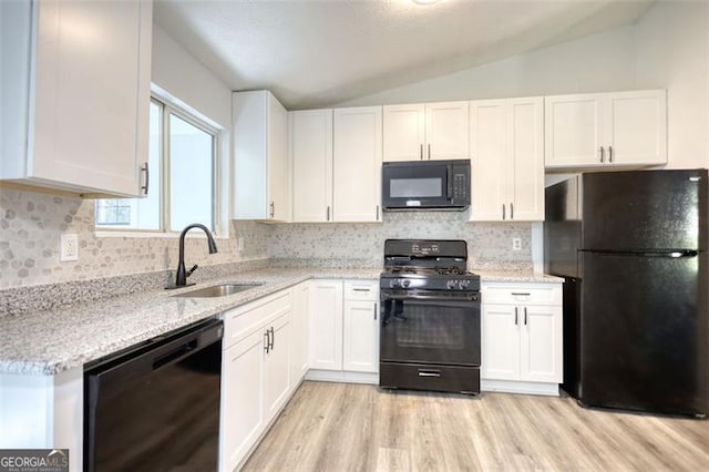 kitchen featuring black appliances, a sink, vaulted ceiling, light wood-type flooring, and white cabinetry
