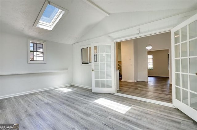 unfurnished room with a skylight, french doors, wood finished floors, and baseboards