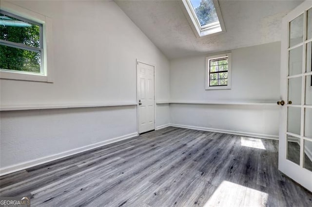 empty room with lofted ceiling, wood finished floors, a skylight, and baseboards