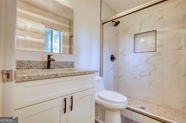 full bath featuring toilet, a marble finish shower, and vanity
