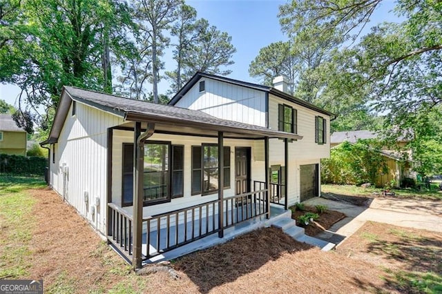 view of front facade featuring a porch, concrete driveway, a chimney, and a garage