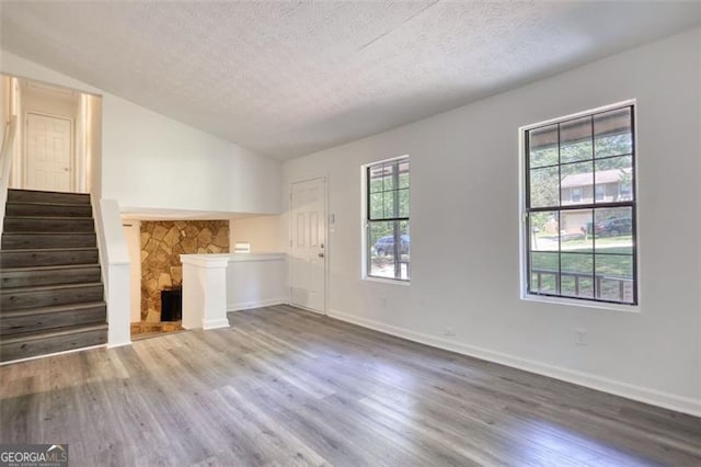 unfurnished living room featuring wood finished floors, a textured ceiling, lofted ceiling, stairway, and baseboards