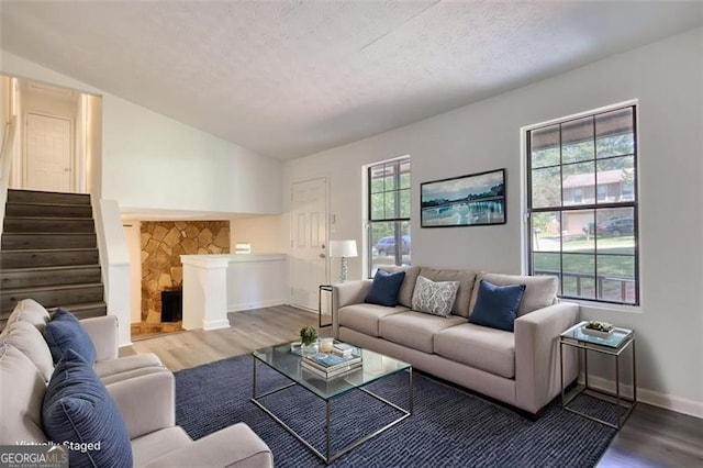 living area featuring wood finished floors, vaulted ceiling, baseboards, stairs, and a textured ceiling