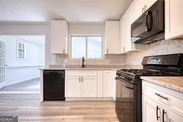 kitchen featuring black appliances, decorative backsplash, light wood-style flooring, and a sink