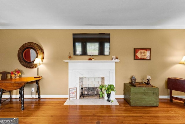 living area featuring crown molding, wood finished floors, baseboards, and a fireplace with flush hearth