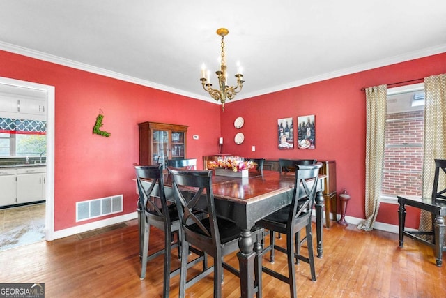 dining room with a chandelier, healthy amount of natural light, wood finished floors, and ornamental molding