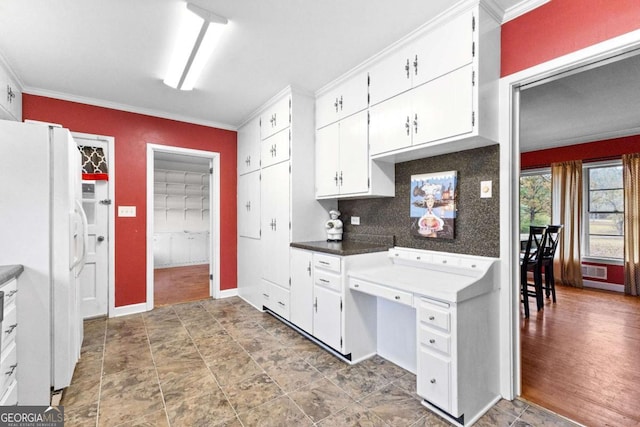 kitchen featuring freestanding refrigerator, ornamental molding, white cabinets, baseboards, and dark countertops