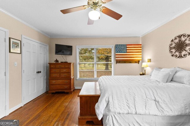 bedroom featuring crown molding, wood finished floors, baseboards, a ceiling fan, and a closet
