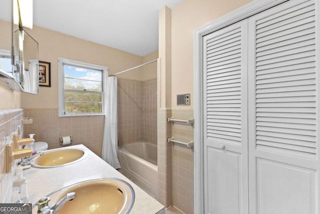 full bath with tile walls, a closet, shower / bathtub combination with curtain, a wainscoted wall, and double vanity