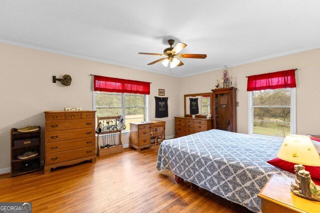 bedroom with wood finished floors, multiple windows, crown molding, baseboards, and ceiling fan