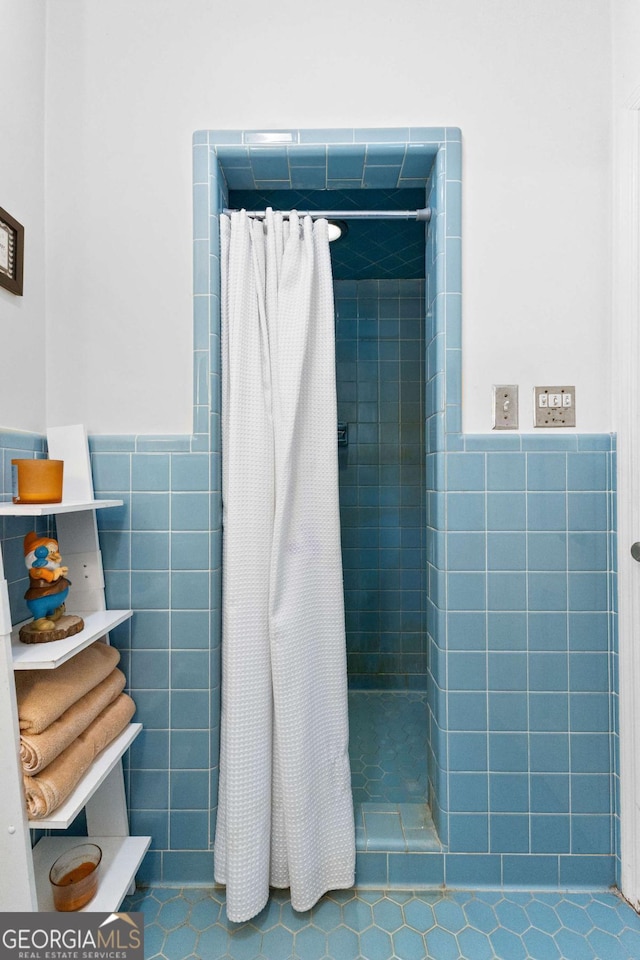 bathroom with tile walls, tile patterned floors, a tile shower, and wainscoting