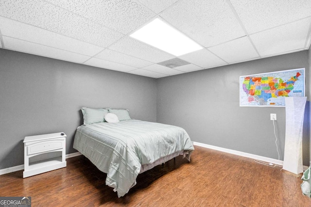 bedroom with wood finished floors, baseboards, and a drop ceiling