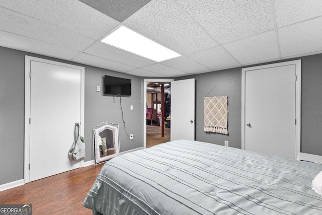 bedroom featuring a drop ceiling, wood finished floors, and baseboards