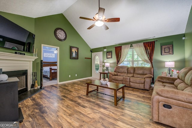 living area featuring ceiling fan, high vaulted ceiling, wood finished floors, a fireplace with raised hearth, and baseboards