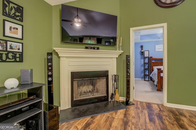 living room with a fireplace with raised hearth, wood finished floors, baseboards, and a ceiling fan
