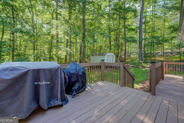 wooden deck featuring a storage shed, an outdoor structure, a grill, and a forest view