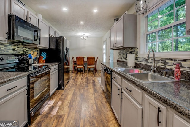 kitchen featuring black appliances, a sink, a textured ceiling, tasteful backsplash, and wood finished floors