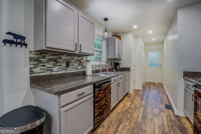 kitchen with dishwasher, a sink, dark wood-style flooring, dark countertops, and decorative backsplash