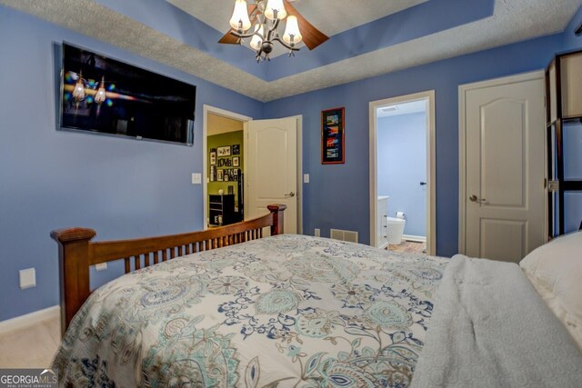 bedroom featuring baseboards, a chandelier, ensuite bath, carpet floors, and a raised ceiling