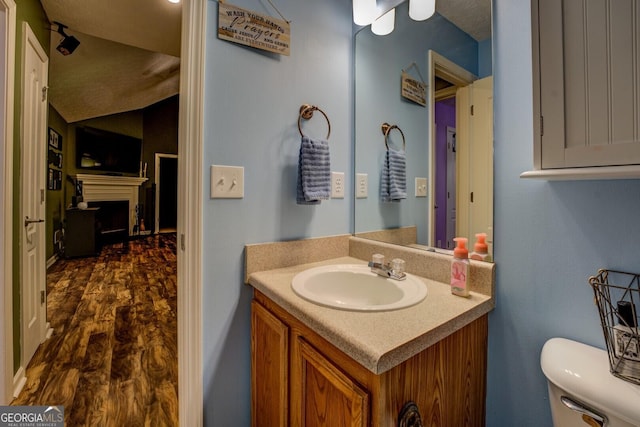 half bathroom featuring toilet, vanity, vaulted ceiling, and a fireplace