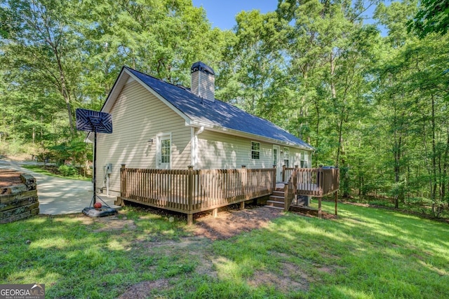 rear view of property with a chimney, a lawn, and a wooden deck