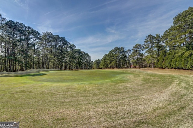 view of community featuring golf course view, a yard, and view of wooded area