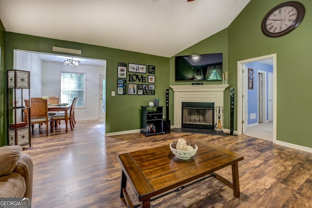 living room featuring wood finished floors, a fireplace with flush hearth, baseboards, vaulted ceiling, and a ceiling fan