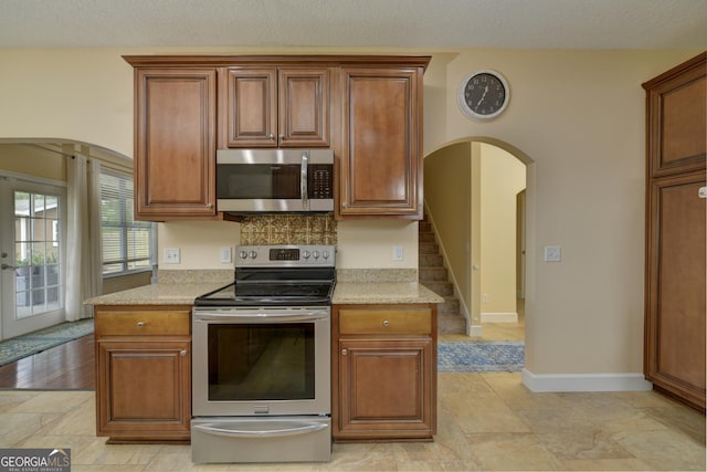 506 Hide Away Lake Loop, Kingsland, GA 31548 - kitchen featuring stainless steel appliances, arched walkways, baseboards, brown cabinetry, and a textured ceiling