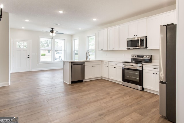 kitchen featuring appliances with stainless steel finishes, a sink, a peninsula, white cabinetry, and recessed lighting