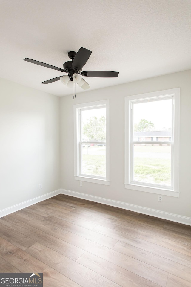 empty room with baseboards, wood finished floors, plenty of natural light, and a ceiling fan