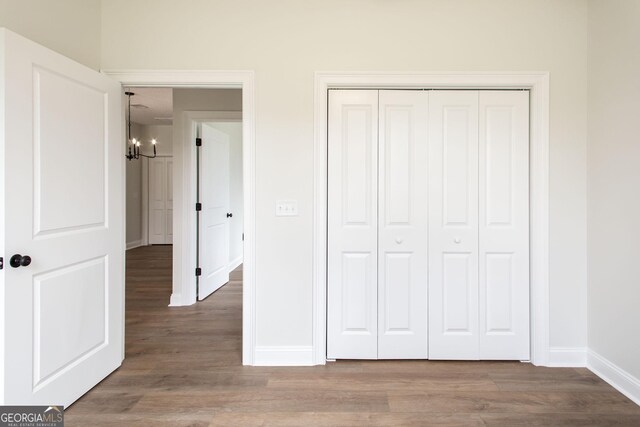 unfurnished bedroom featuring a chandelier, baseboards, wood finished floors, and a closet