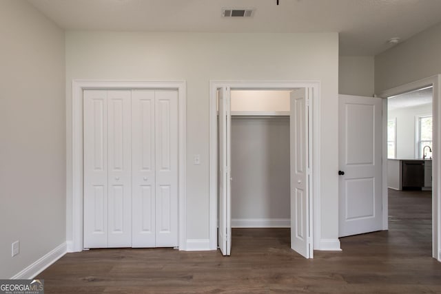 unfurnished bedroom featuring dark wood-style flooring, baseboards, two closets, and a sink