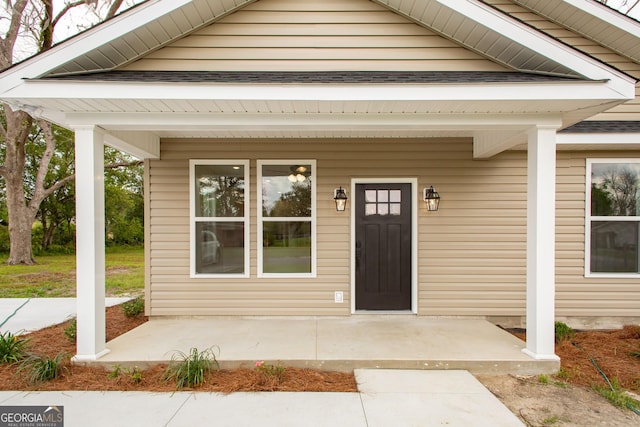 view of exterior entry with a porch and a shingled roof