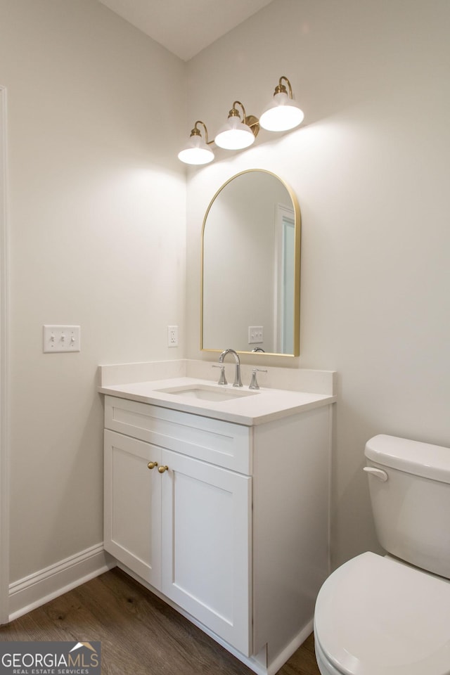 half bath with vanity, wood finished floors, toilet, and baseboards