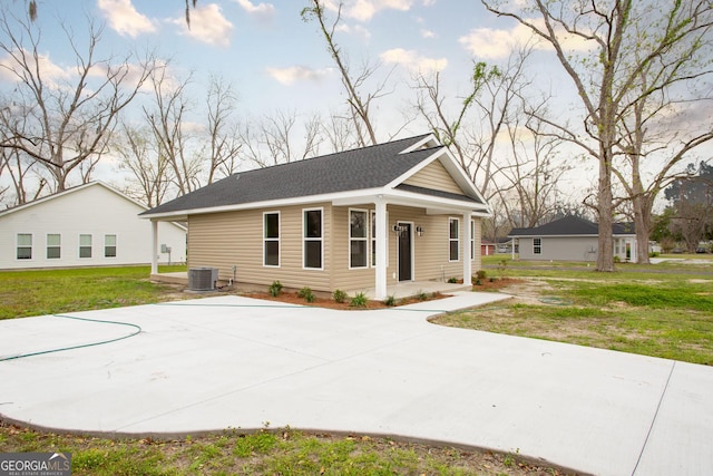view of front of property with a front lawn, cooling unit, and roof with shingles