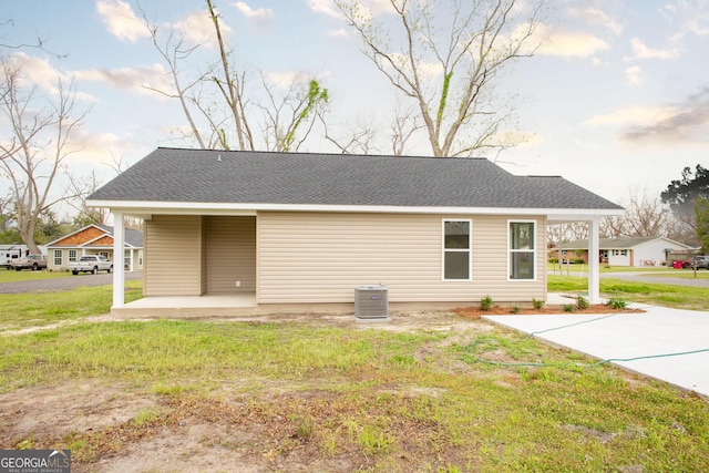 rear view of property featuring central AC unit, a lawn, and roof with shingles