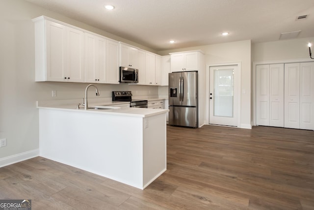 kitchen with stainless steel appliances, a sink, wood finished floors, light countertops, and recessed lighting