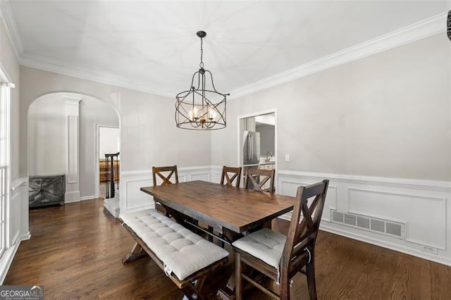 5652 Harbormist Dr, Powder Springs, GA 30127 - dining space featuring arched walkways, dark wood finished floors, a chandelier, a wainscoted wall, and ornamental molding