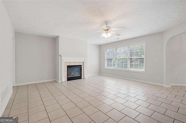 unfurnished living room featuring a textured ceiling, a ceiling fan, a tiled fireplace, arched walkways, and baseboards